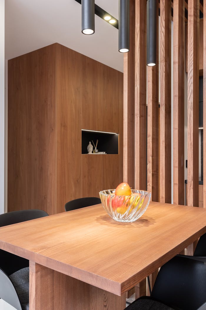 Glass vase with fresh fruits placed on wooden table in stylish minimalist dining room